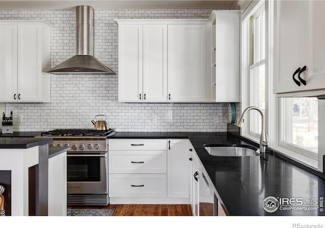 kitchen featuring wall chimney exhaust hood, dark wood-type flooring, high end range, sink, and white cabinets