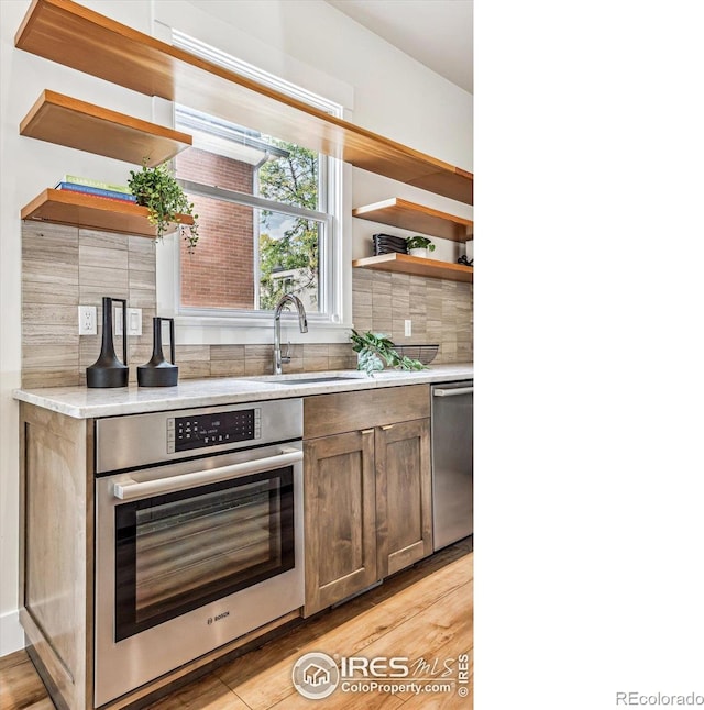 kitchen with sink, appliances with stainless steel finishes, light wood-type flooring, and tasteful backsplash