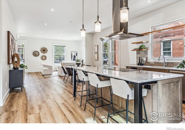 kitchen with island range hood, light hardwood / wood-style flooring, sink, pendant lighting, and a center island