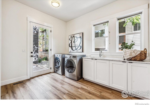 washroom with light hardwood / wood-style flooring, washer and clothes dryer, a healthy amount of sunlight, and cabinets