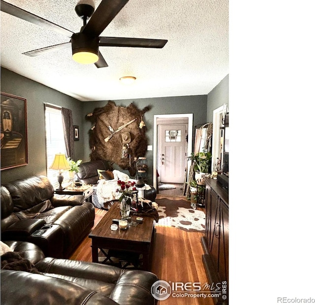 living room with a textured ceiling, dark wood-type flooring, and ceiling fan