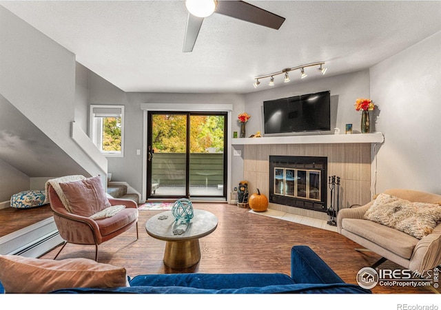living area featuring a fireplace, wood finished floors, a baseboard radiator, and a ceiling fan
