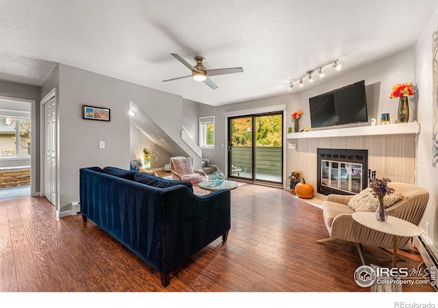 living room with ceiling fan, a textured ceiling, dark hardwood / wood-style flooring, and a tile fireplace