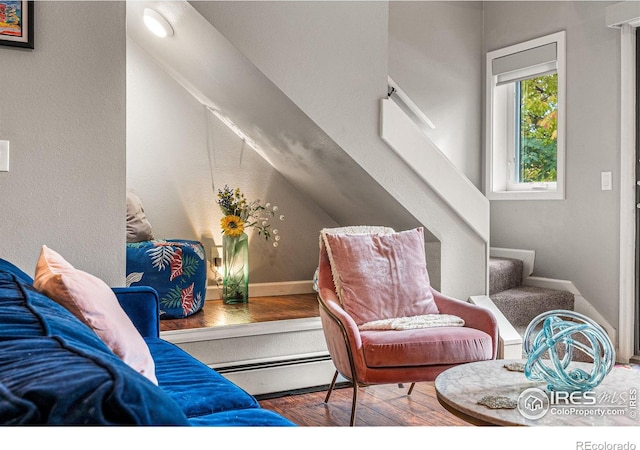 living area with hardwood / wood-style flooring, a baseboard heating unit, and stairs