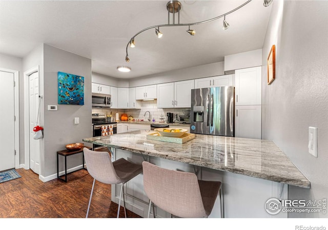 kitchen with white cabinets, dark wood finished floors, light stone countertops, appliances with stainless steel finishes, and a breakfast bar area