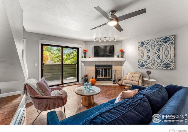 living area with a ceiling fan, wood finished floors, a textured ceiling, a tiled fireplace, and baseboards