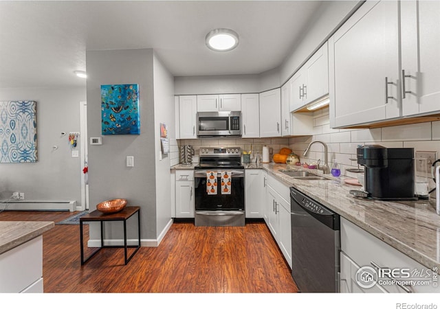 kitchen featuring dark wood finished floors, stainless steel appliances, a sink, a baseboard heating unit, and decorative backsplash
