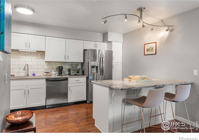kitchen with dishwasher, a sink, decorative backsplash, stainless steel fridge, and a breakfast bar area
