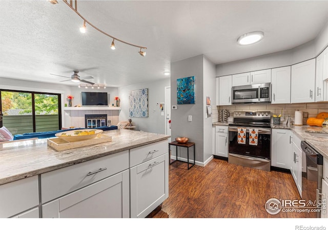 kitchen featuring decorative backsplash, dark hardwood / wood-style floors, white cabinetry, appliances with stainless steel finishes, and light stone counters