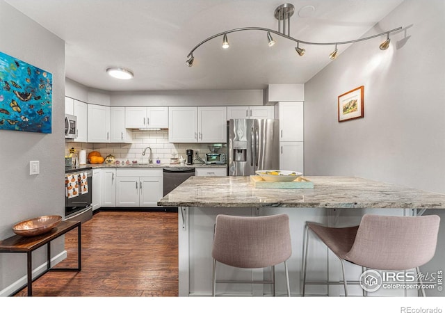 kitchen featuring dark wood-type flooring, stainless steel appliances, white cabinetry, light stone counters, and tasteful backsplash