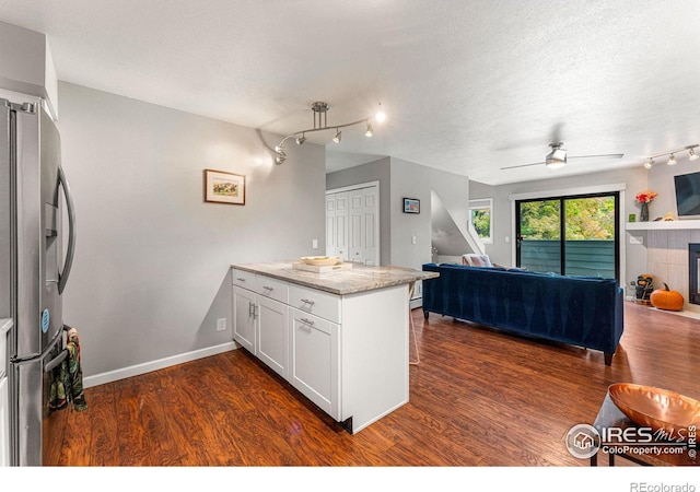 kitchen featuring dark hardwood / wood-style flooring, white cabinetry, light stone countertops, and stainless steel refrigerator