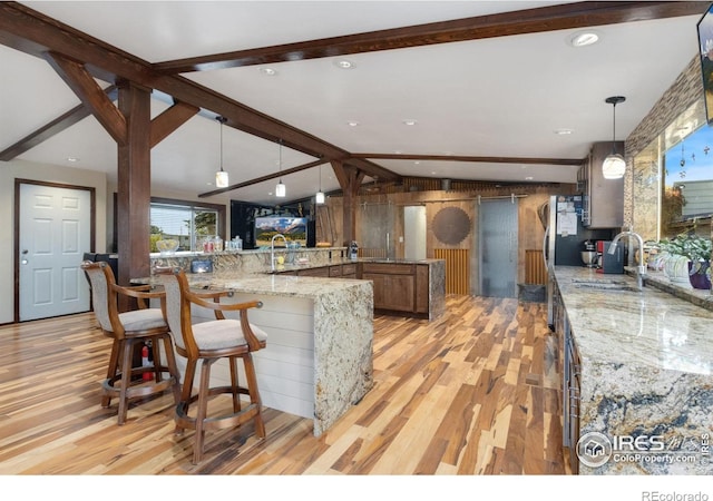 kitchen featuring kitchen peninsula, light stone counters, pendant lighting, light hardwood / wood-style floors, and sink