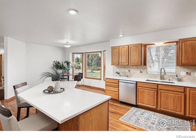 kitchen featuring tasteful backsplash, a kitchen island, light wood-type flooring, dishwasher, and sink