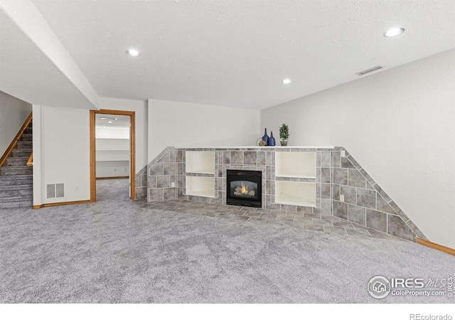 unfurnished living room with a textured ceiling, carpet flooring, and a tile fireplace