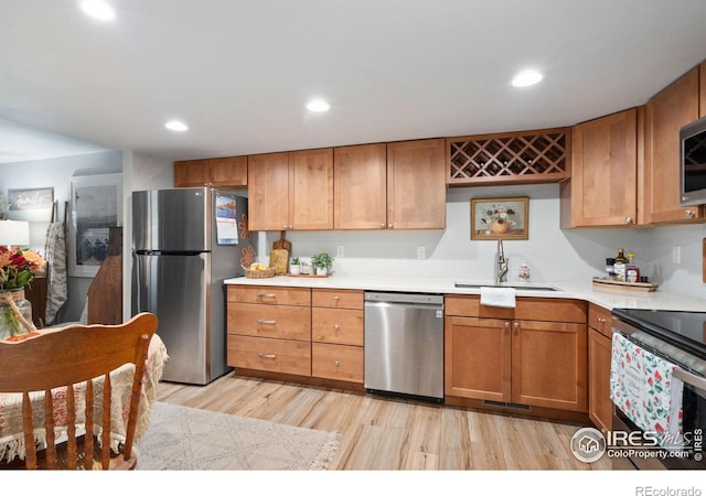 kitchen with appliances with stainless steel finishes, sink, and light wood-type flooring