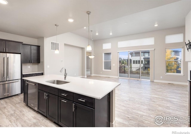 kitchen featuring a center island with sink, appliances with stainless steel finishes, light hardwood / wood-style flooring, sink, and decorative light fixtures