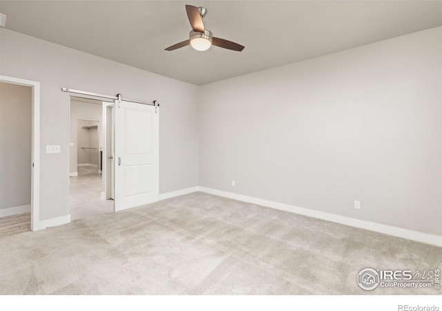 unfurnished bedroom featuring a closet, a spacious closet, a barn door, light colored carpet, and ceiling fan