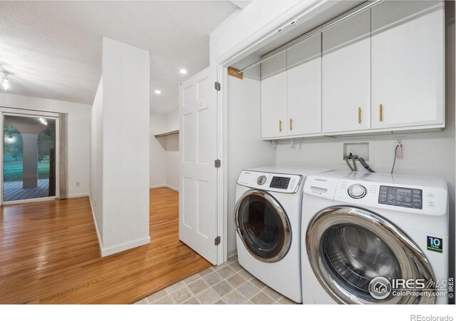 clothes washing area with light hardwood / wood-style floors, cabinets, separate washer and dryer, and a textured ceiling