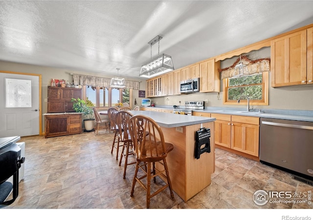 kitchen with a kitchen island, a kitchen breakfast bar, hanging light fixtures, sink, and appliances with stainless steel finishes