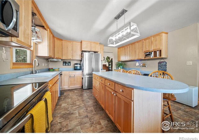 kitchen with sink, a center island, a breakfast bar, pendant lighting, and appliances with stainless steel finishes