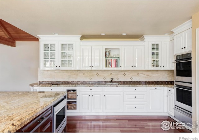 kitchen with dark hardwood / wood-style floors, white cabinets, appliances with stainless steel finishes, light stone counters, and tasteful backsplash