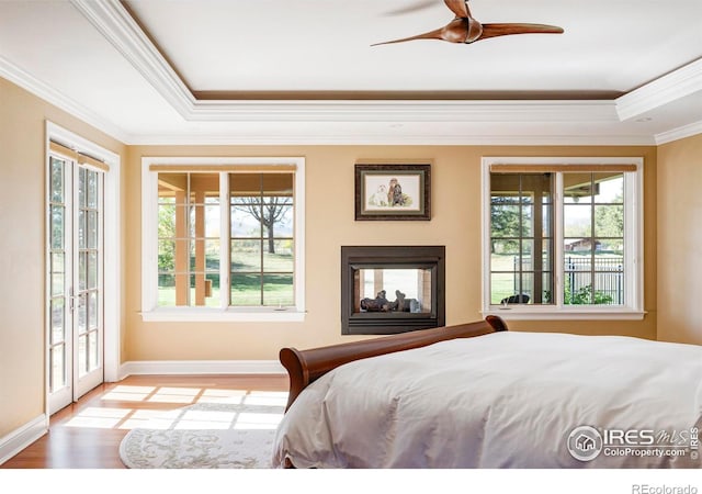 bedroom with ceiling fan, access to outside, a tray ceiling, light hardwood / wood-style floors, and crown molding