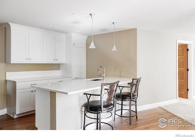 kitchen with white cabinets, sink, hanging light fixtures, and light wood-type flooring