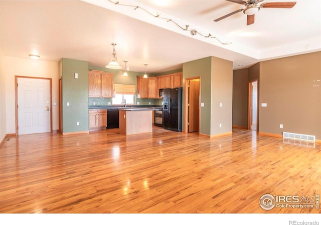 kitchen with a kitchen island, black appliances, pendant lighting, light wood-type flooring, and tasteful backsplash