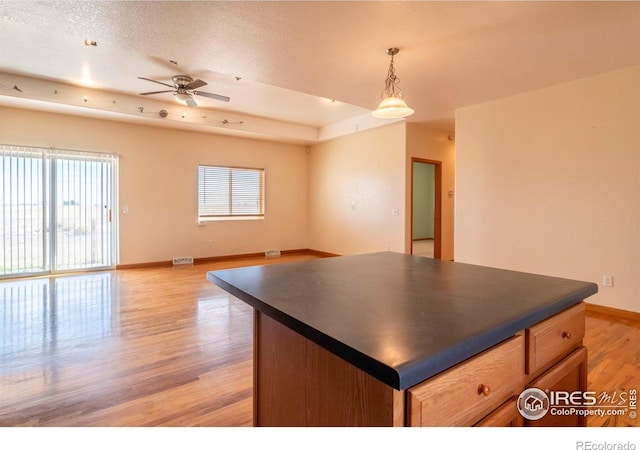 kitchen with ceiling fan, a kitchen island, a textured ceiling, light hardwood / wood-style floors, and decorative light fixtures