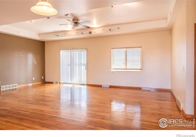 unfurnished room featuring a tray ceiling, light wood-type flooring, and ceiling fan