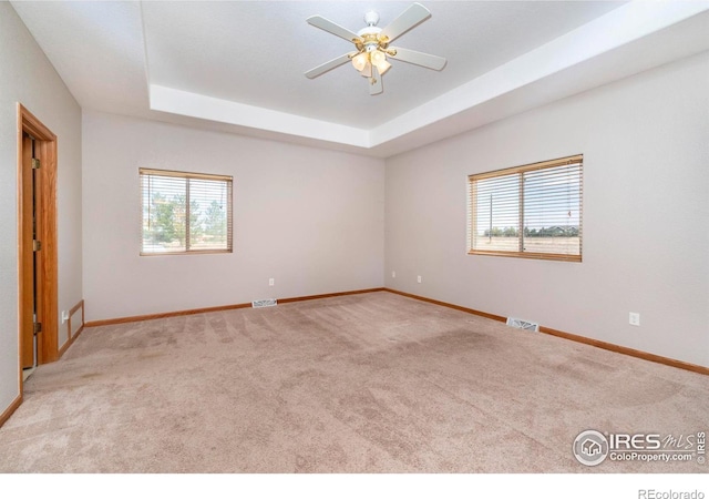 carpeted spare room featuring ceiling fan, a raised ceiling, and a wealth of natural light