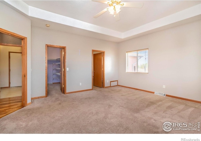 unfurnished bedroom featuring a closet, ceiling fan, light carpet, and a walk in closet