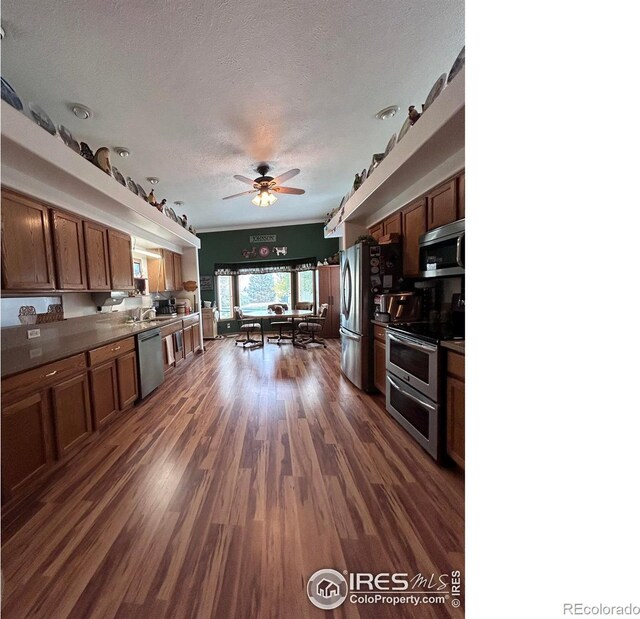 kitchen with dark wood-type flooring, dark countertops, a textured ceiling, appliances with stainless steel finishes, and ceiling fan