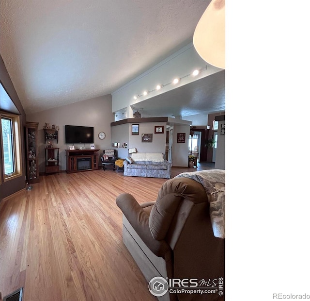 living room with a fireplace, vaulted ceiling, wood finished floors, and visible vents