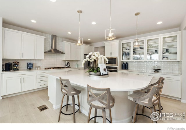 kitchen with white cabinetry, a large island with sink, wall chimney exhaust hood, and decorative light fixtures