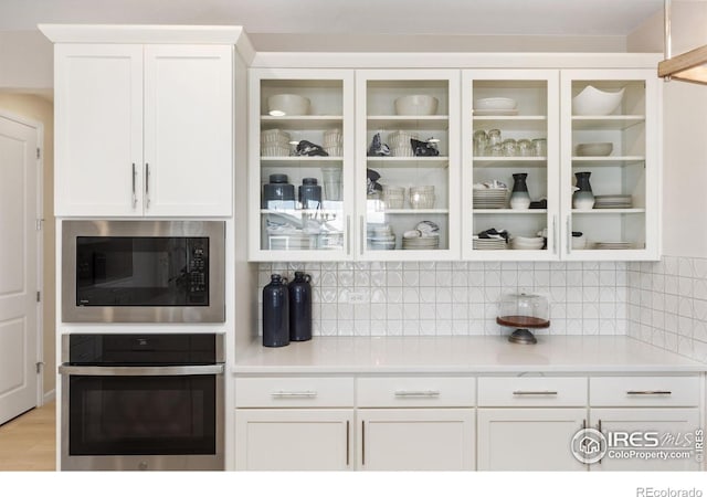 kitchen featuring decorative backsplash, stainless steel oven, white cabinetry, light wood-type flooring, and built in microwave