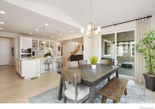 dining area with light hardwood / wood-style flooring, vaulted ceiling, and a chandelier