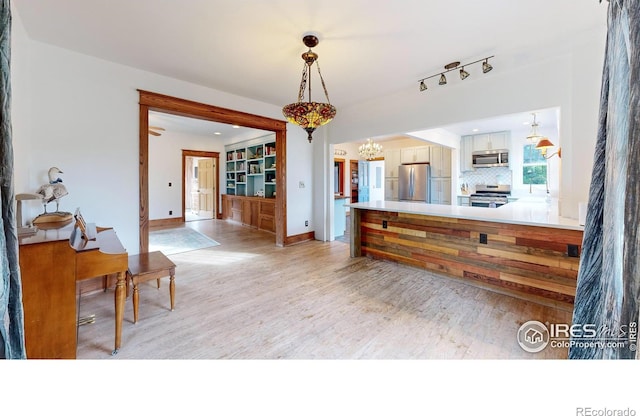 kitchen featuring tasteful backsplash, stainless steel appliances, decorative light fixtures, white cabinets, and light hardwood / wood-style floors