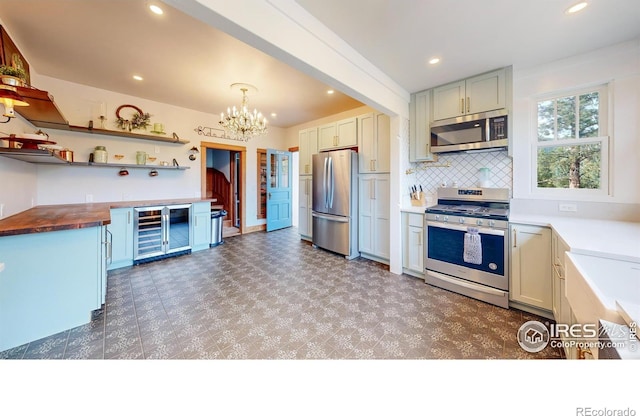 kitchen with beverage cooler, butcher block countertops, a chandelier, pendant lighting, and appliances with stainless steel finishes