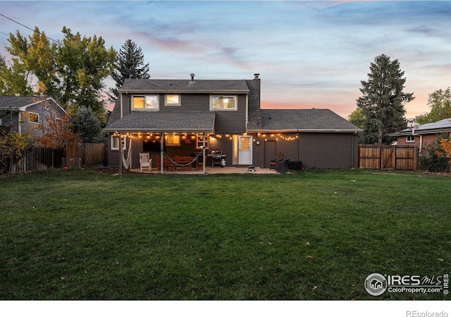 back house at dusk featuring a patio area and a yard