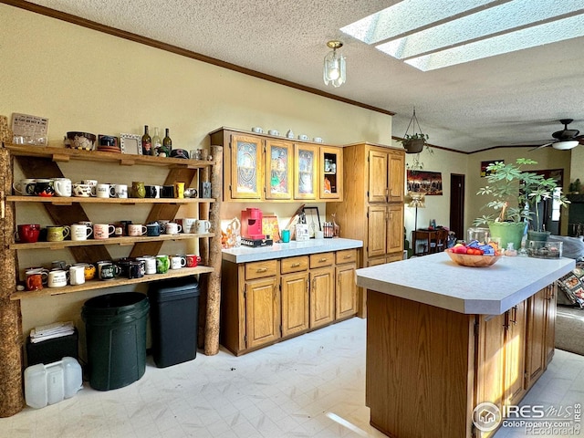 kitchen featuring a center island, crown molding, a skylight, ceiling fan, and a textured ceiling