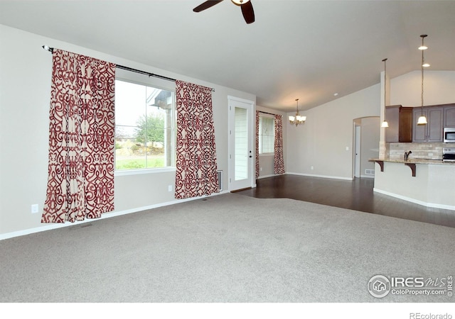 unfurnished living room with lofted ceiling, ceiling fan with notable chandelier, and dark hardwood / wood-style flooring