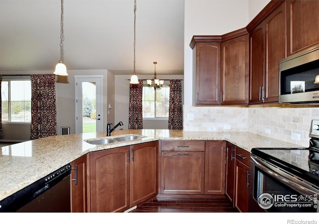 kitchen with hanging light fixtures, light stone counters, dark wood-type flooring, sink, and stainless steel appliances