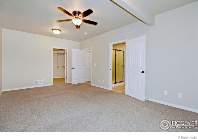 unfurnished bedroom featuring light carpet, a walk in closet, a closet, and ceiling fan