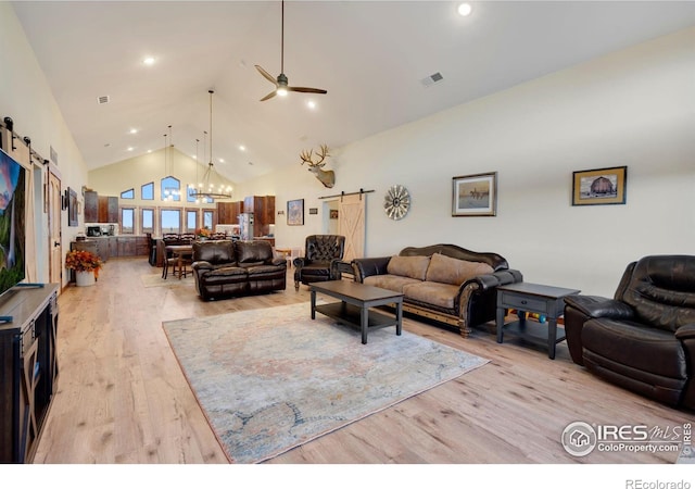 living room with light hardwood / wood-style floors, a barn door, high vaulted ceiling, and ceiling fan with notable chandelier