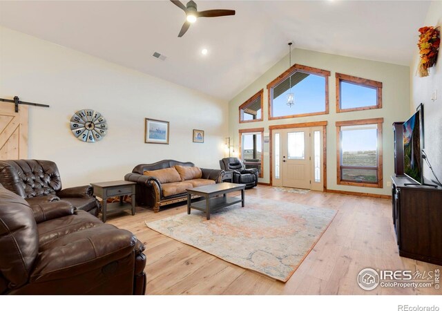 living room with light hardwood / wood-style flooring, a barn door, high vaulted ceiling, and ceiling fan