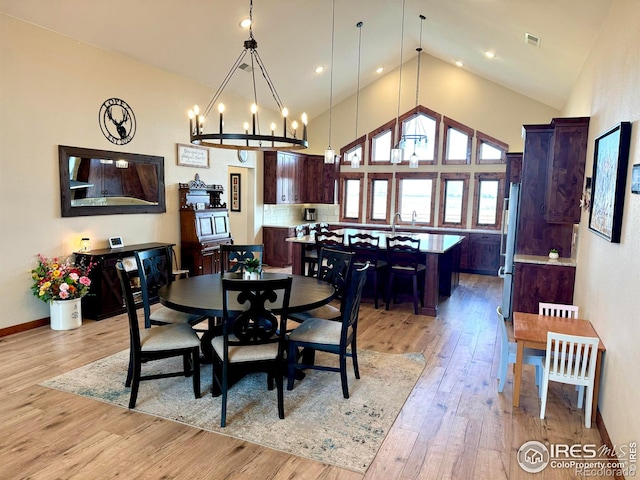 dining area with sink, a notable chandelier, high vaulted ceiling, and light hardwood / wood-style floors