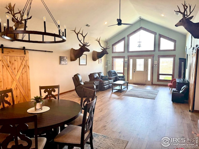 dining room featuring light hardwood / wood-style floors, a barn door, high vaulted ceiling, and ceiling fan