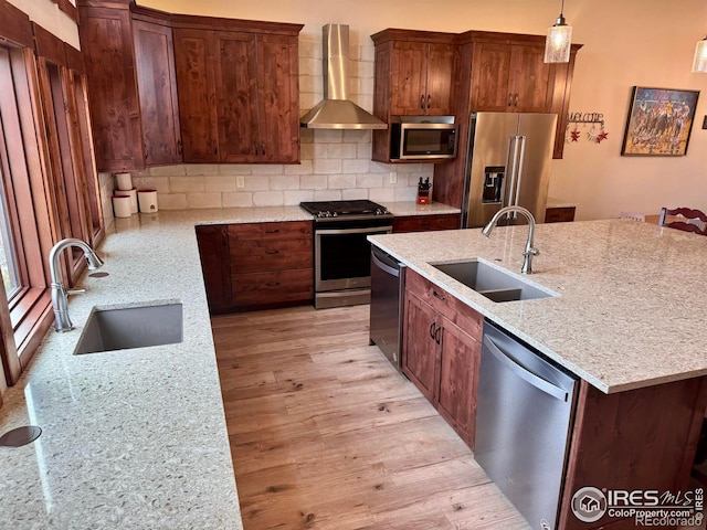 kitchen featuring sink, wall chimney range hood, stainless steel appliances, and light wood-type flooring