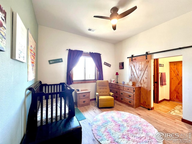 bedroom with ceiling fan, light hardwood / wood-style flooring, a barn door, and a crib